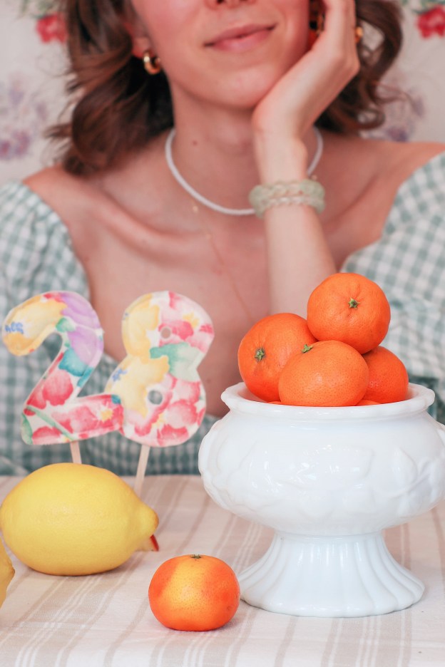 A girl sits at a table with a bowl of fruit in front of her.