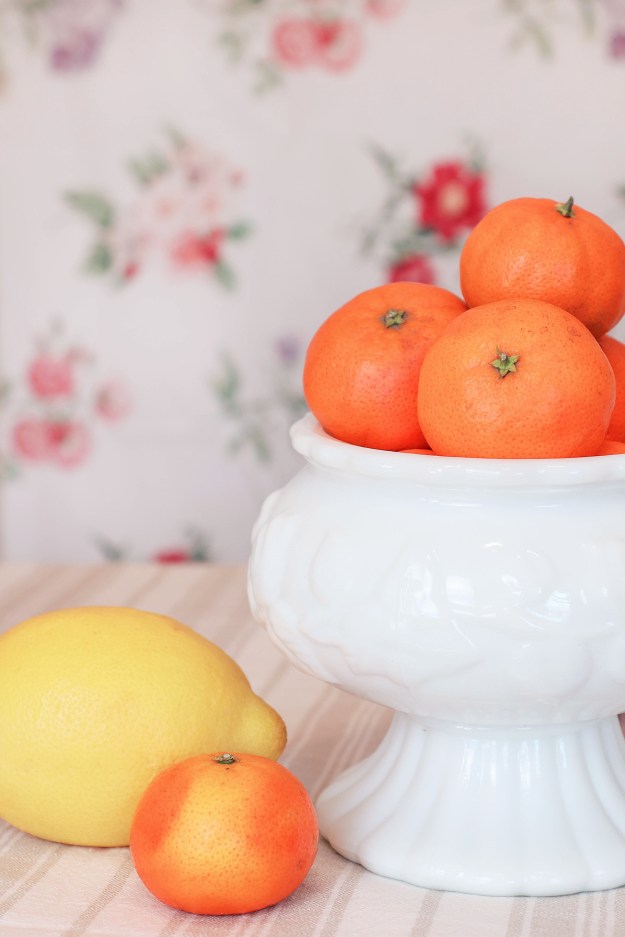 A bowl of oranges sit next to a lemon.