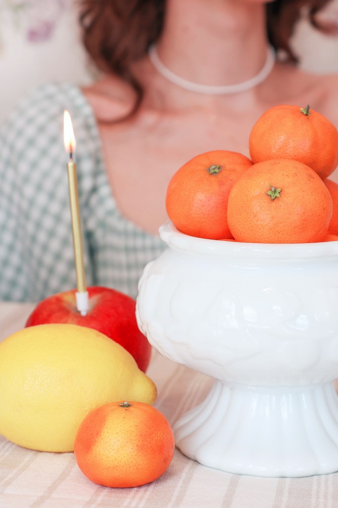 Various fruits sit together on a table. A birthday candle is stuck into the apple.