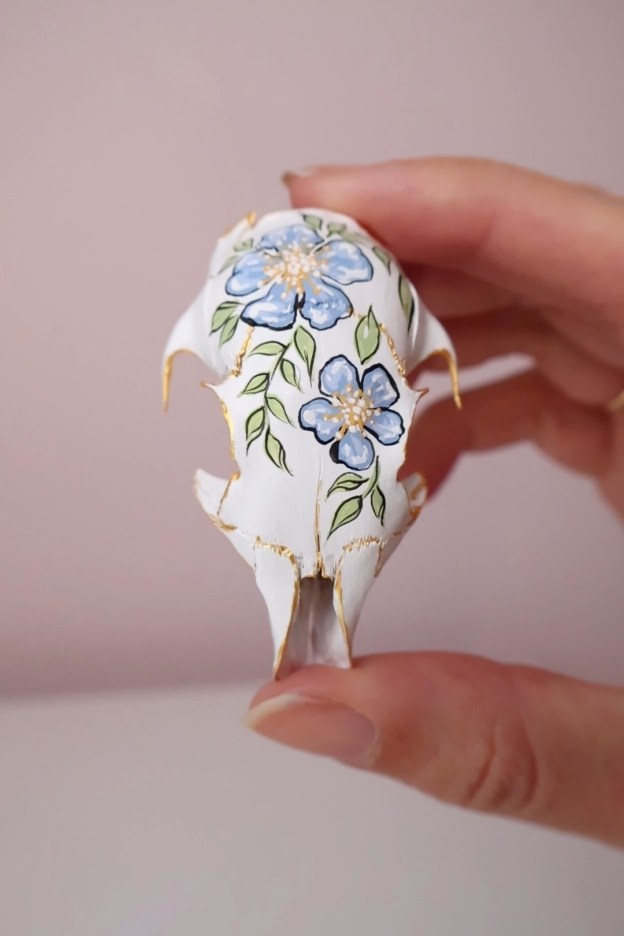 A squirrel skull painted white with blue flowers on it