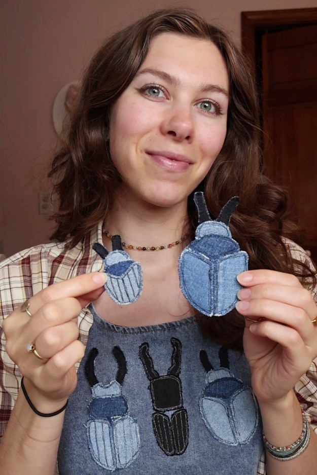 A girl holds up two beetles sewn out of denim