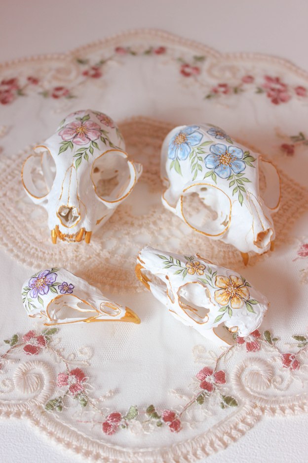 Four painted animal skulls sit on a lace doily